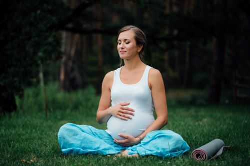 Gravid kvinna sitter i yogaposition utomhus